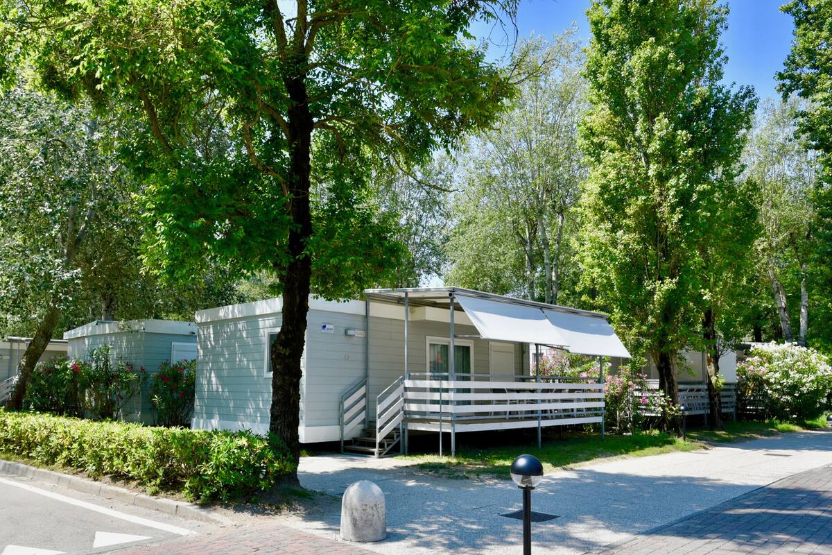A row of mobile homes with a covered porch and a gravel driveway.