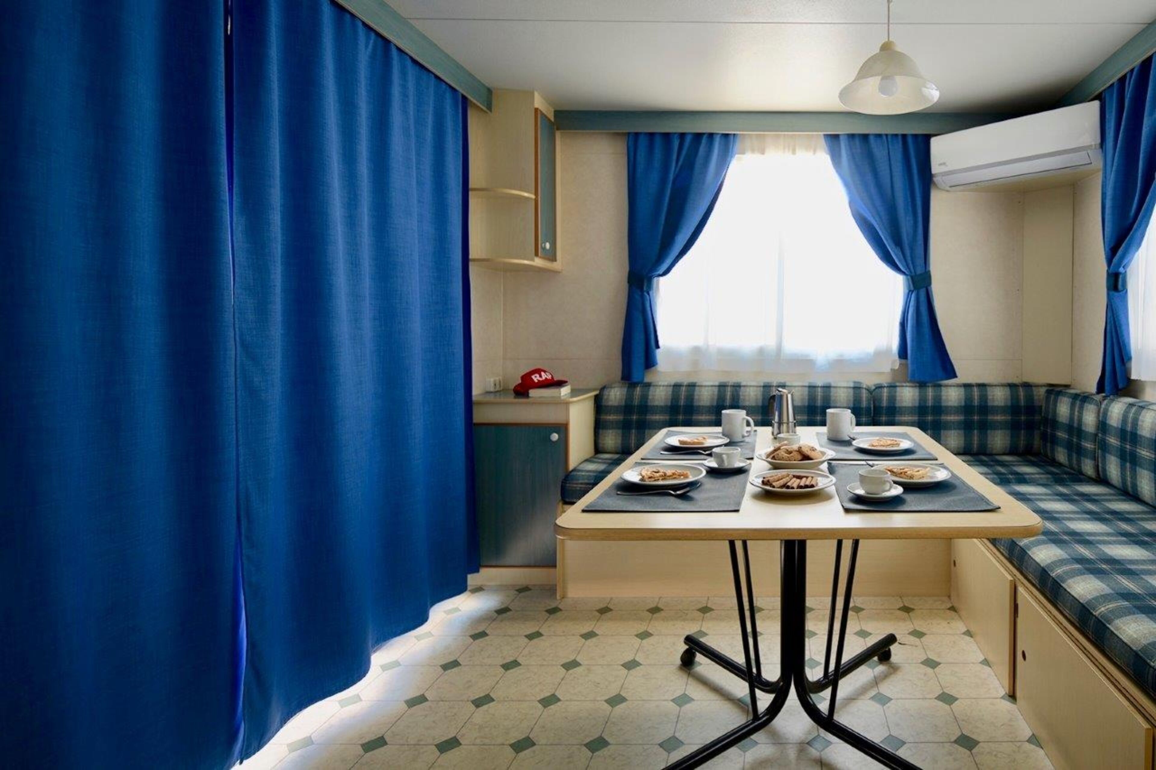 Uma cozinha compacta com mesa de jantar, cortinas azuis e uma janela.