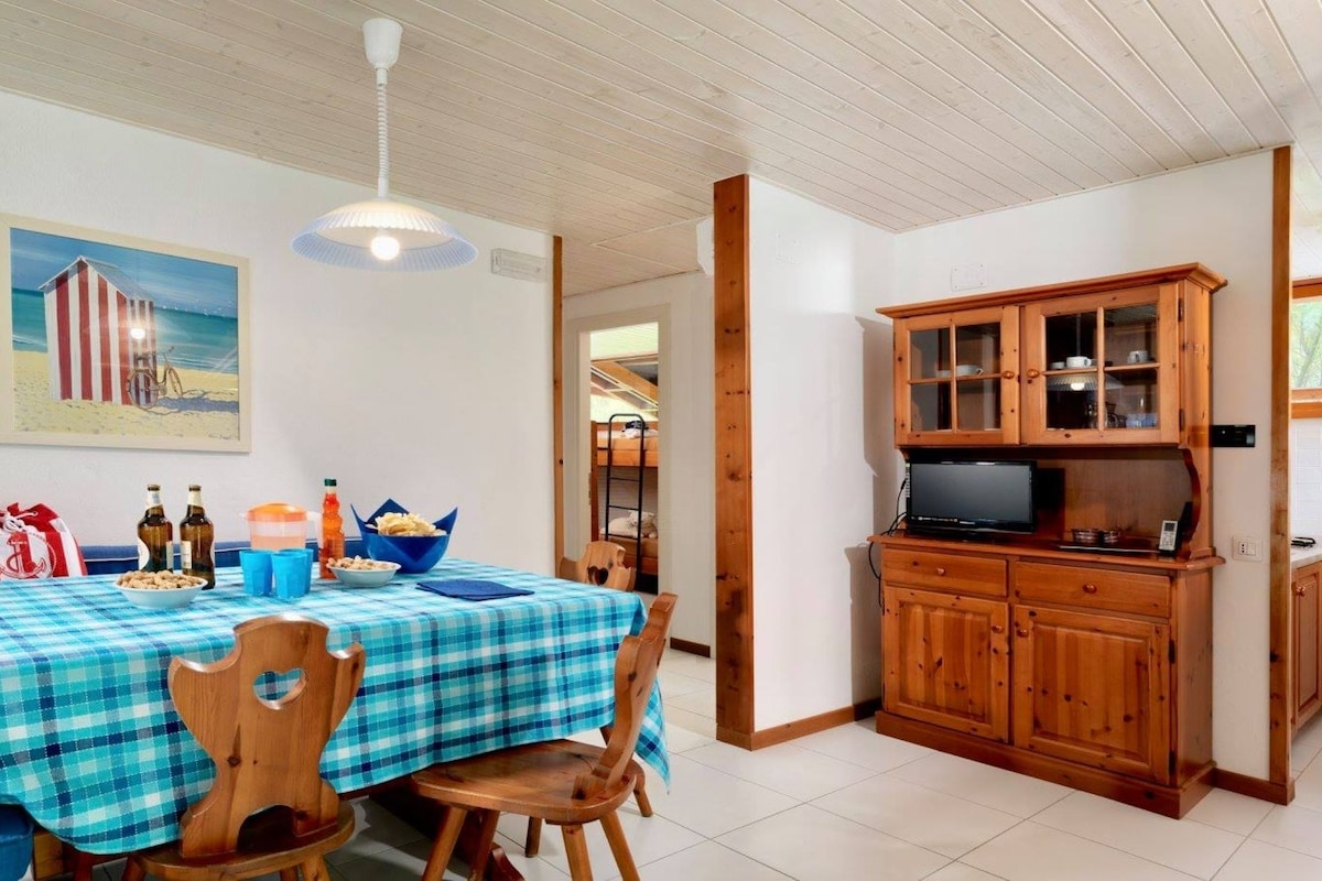 Un coin repas avec une nappe à carreaux, des chaises en bois, un tableau représentant un chalet de plage et un buffet en bois doté de portes en verre.
