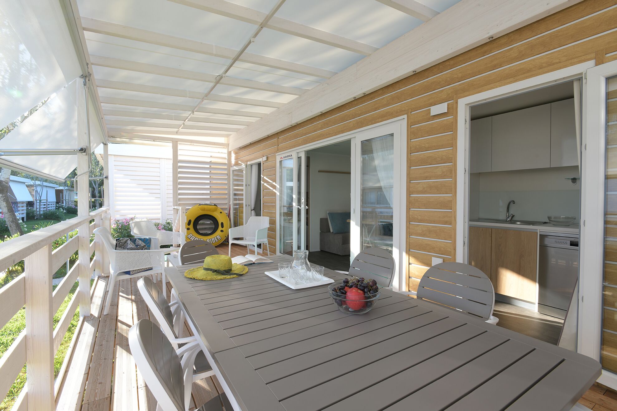 A covered outdoor area with a table and chairs, a kayak, and a kitchen area with cabinets and a sink.