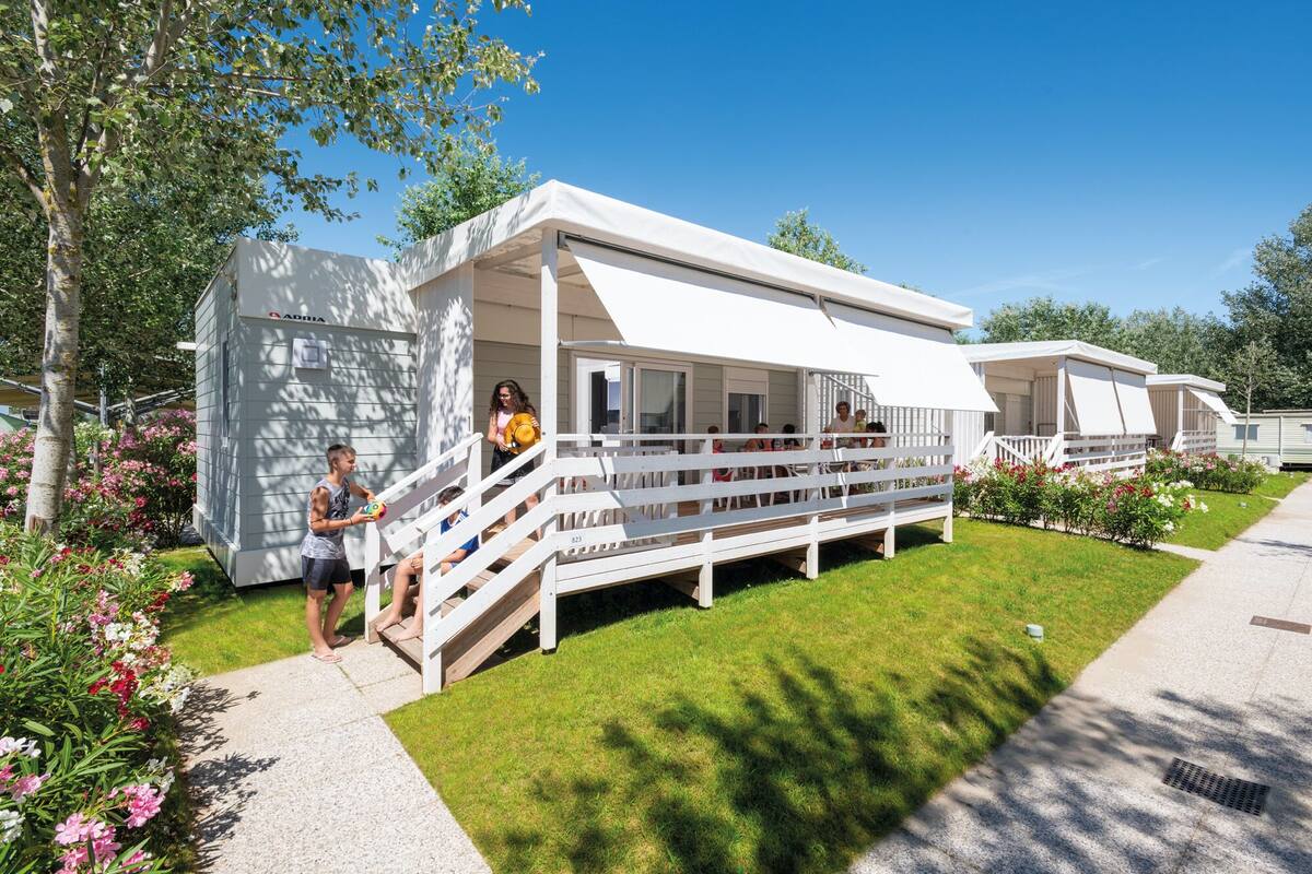 A row of white mobile homes with a grassy lawn and flower beds.