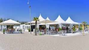 Restaurante à beira-mar com tendas brancas e mesas ao ar livre.