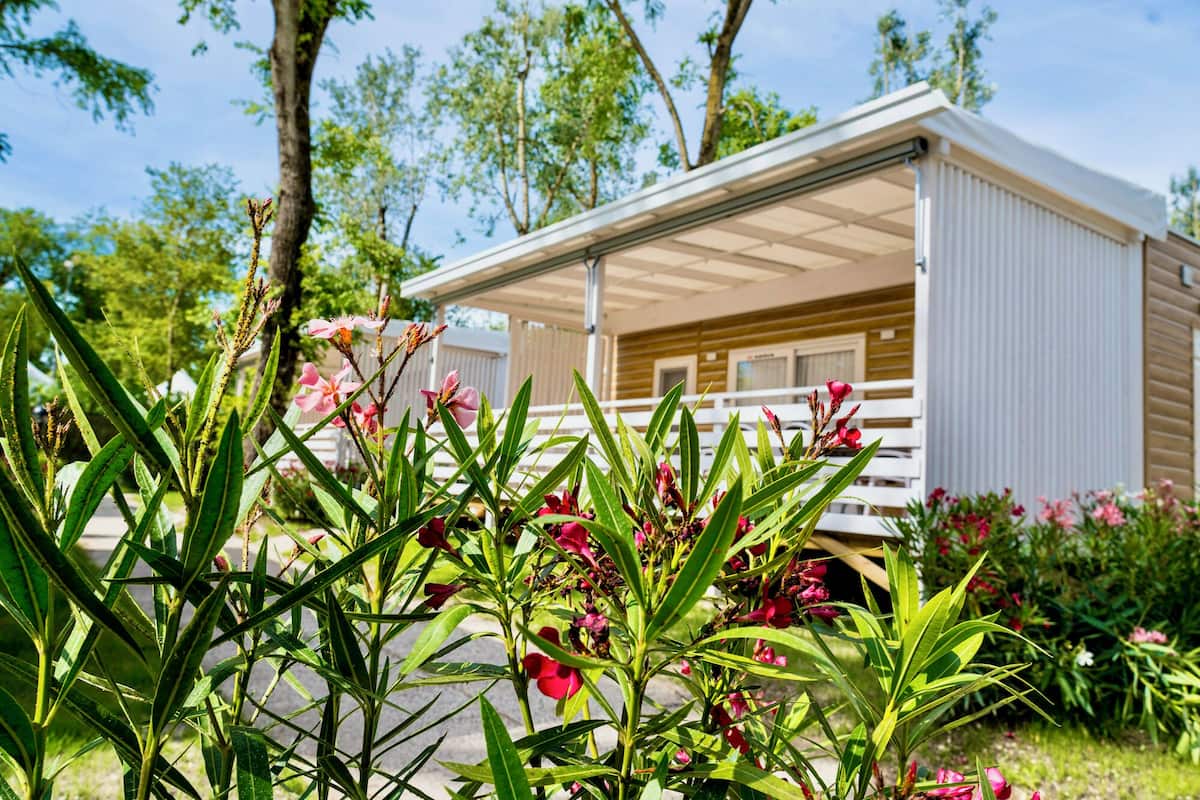 A mobile home with a covered porch and a garden in the foreground.