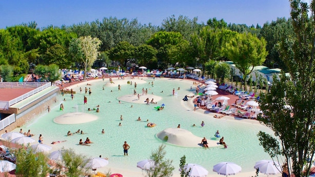 Uma grande piscina ao ar livre com várias pistas, rodeada por espreguiçadeiras e guarda-sóis.