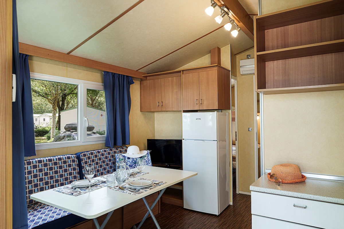 Une cuisine compacte avec des meubles en bois, un réfrigérateur blanc et une table à manger dressée avec des assiettes et des verres.