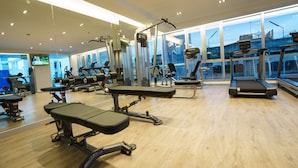Uma academia com diversos equipamentos de ginástica, janelas amplas e piso de madeira.