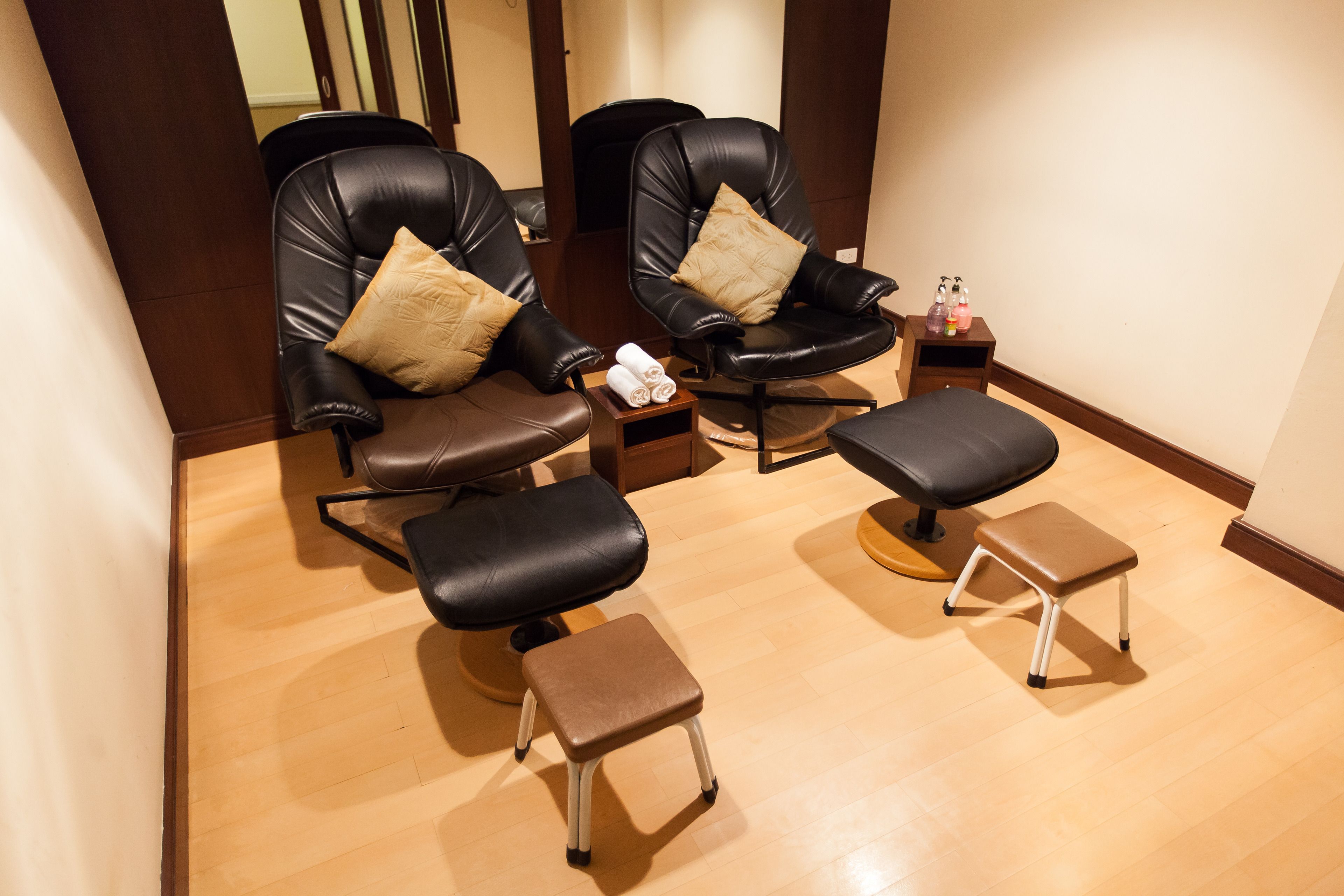 A room with two black leather chairs, each with a beige pillow, and a small wooden stool.