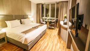 Quarto de hotel com uma cama grande, uma escrivaninha com cadeira, uma televisão e uma janela com cortinas.