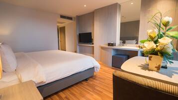 A modern hotel room with a large bed, a desk with a computer, a TV, and a bathroom.