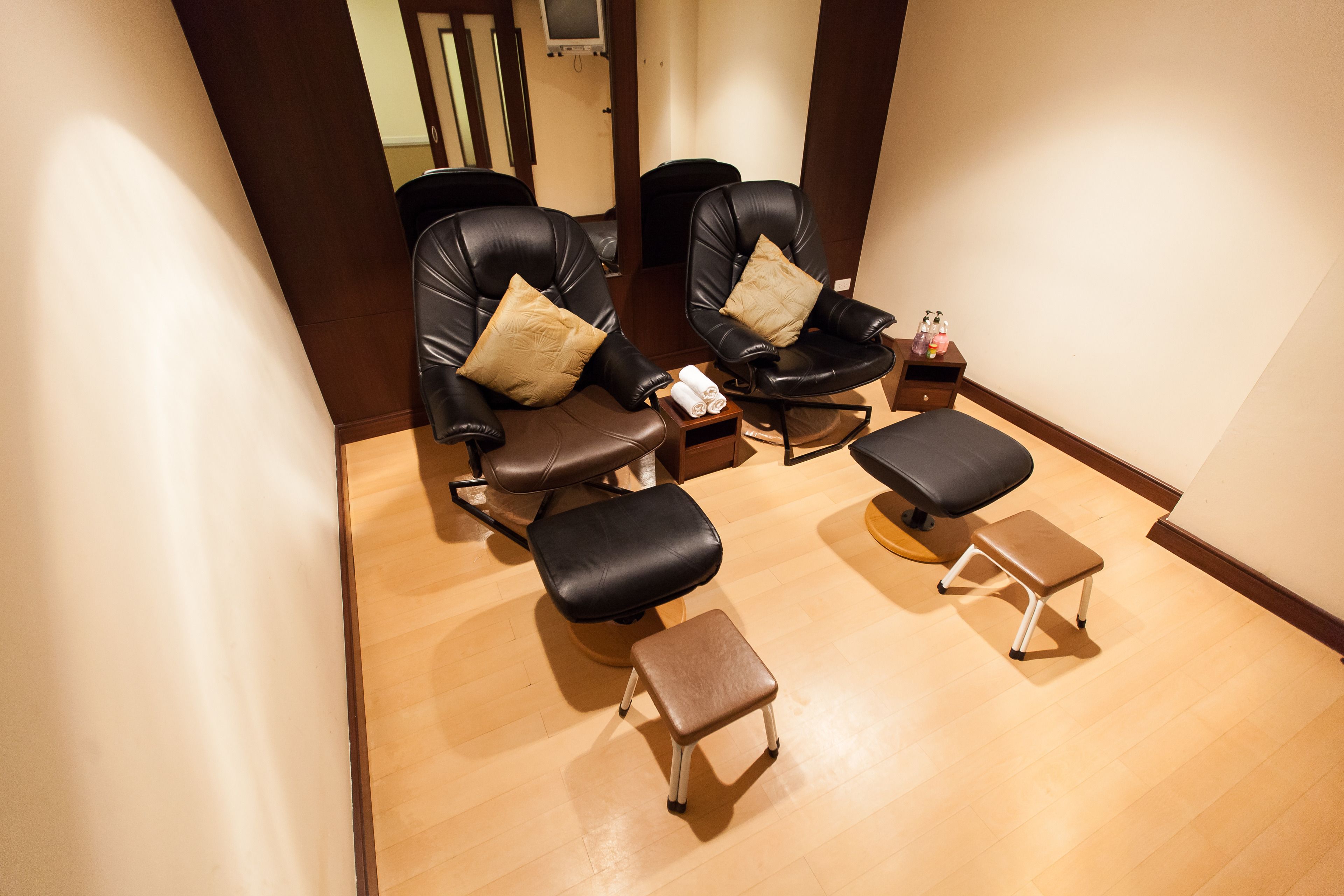 A room with two black leather chairs, each with a matching pillow, and a small wooden stool.