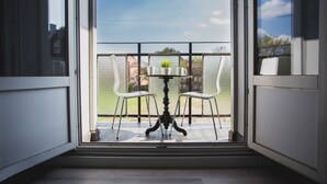 Un balcón con una mesa, dos sillas, una planta en maceta pequeña y vistas al exterior.