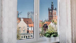 A window with a view of a historic building with a clock tower, a construction crane, and modern buildings in the background.
