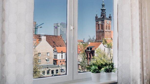 Ventana con vista a un edificio histórico con una torre del reloj, una grúa de construcción y edificios modernos al fondo.