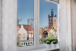 A window with a view of a historic building with a clock tower, a construction crane, and modern buildings in the background. - Midtown Apartments (Gdansk)