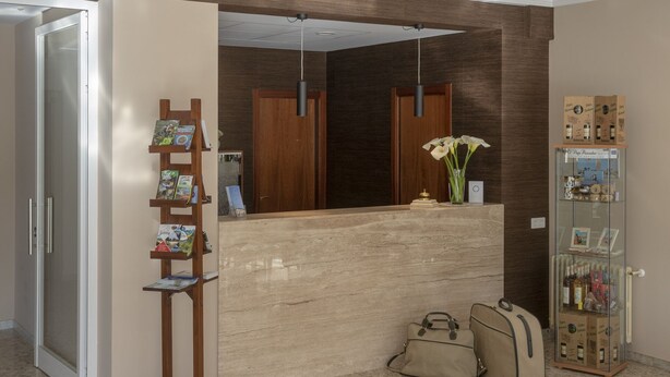 A reception area with a marble floor, a wooden reception desk, a bookshelf, and a circular ceiling light fixture. - Hotel La Ruta (Tapia de Casariego)