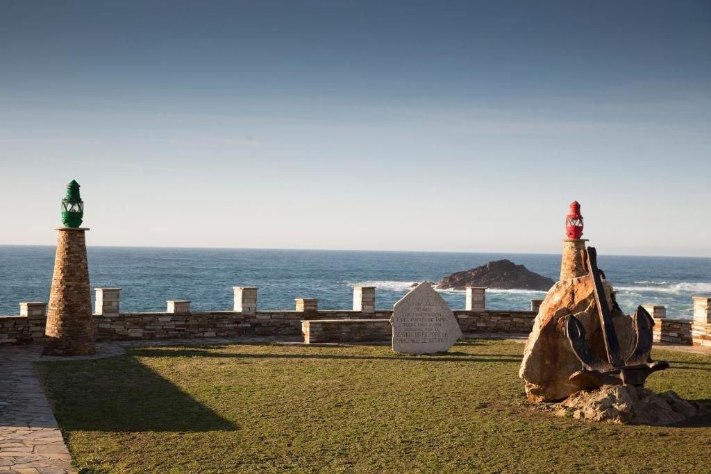 A coastal view with a stone wall, a green lantern, and a red lighthouse.