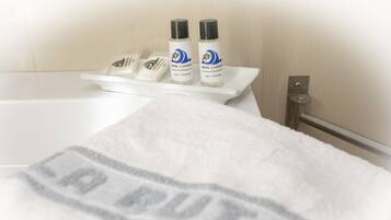 A bathroom with a white towel on a rack, two bottles of Hotel La Ruiti gel and shampoo, and a white bathtub.