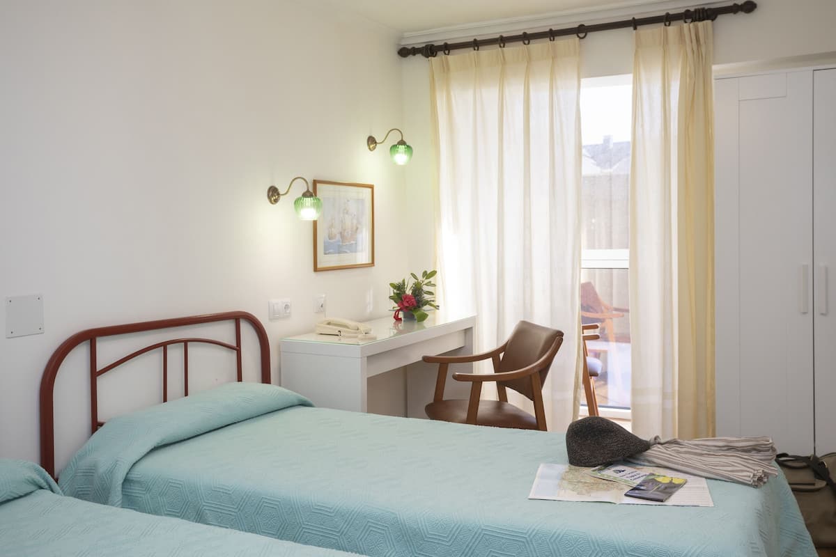 A bedroom with two beds, a desk, a chair, and a window with curtains.