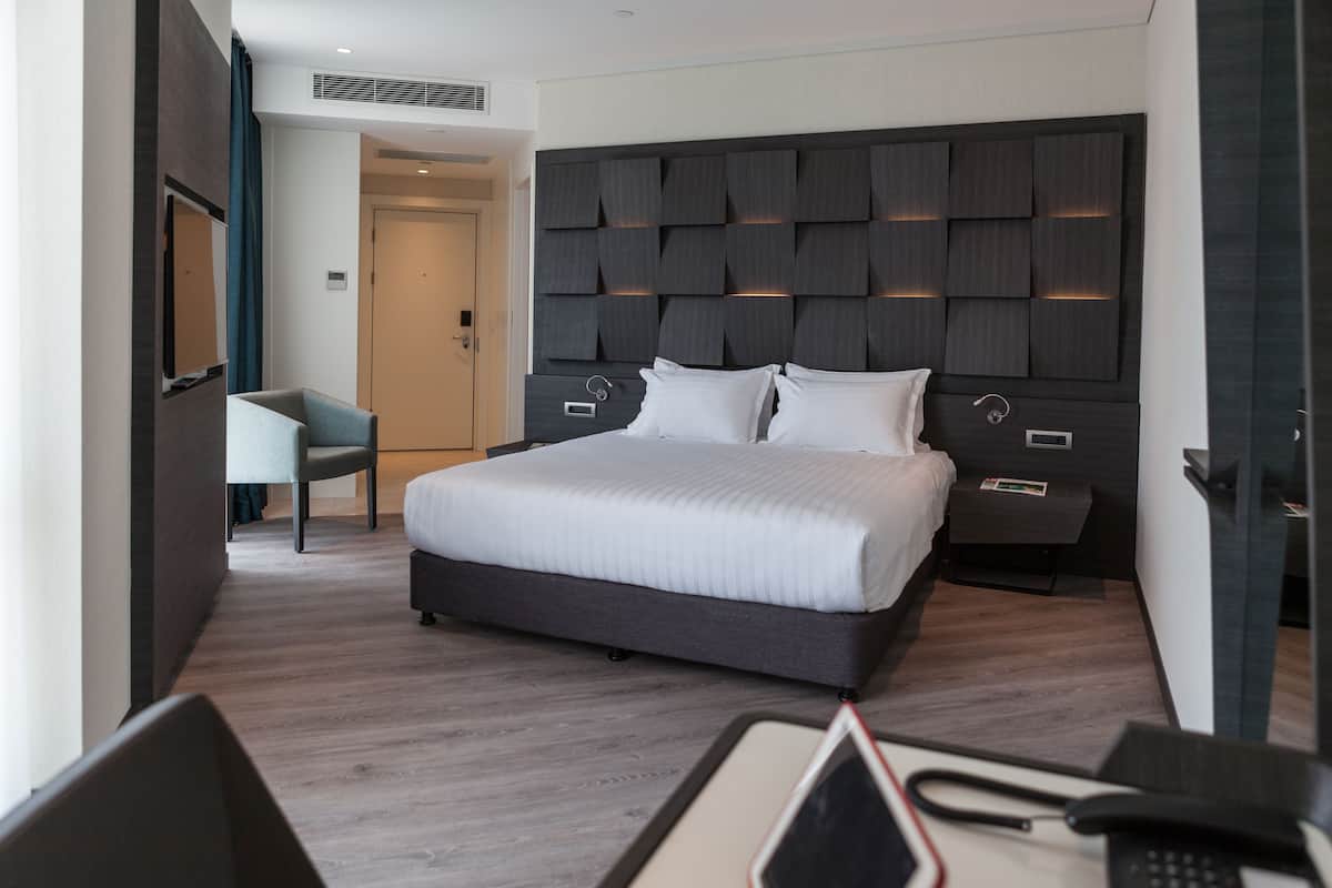 A modern hotel room with a large bed, a desk with a chair, and a TV.