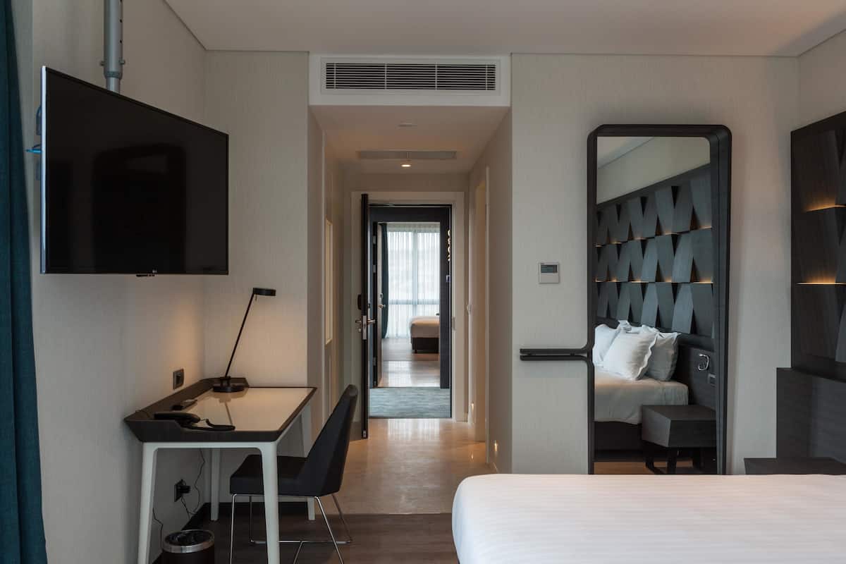 A hotel room with a bed, a desk with a chair, a TV, and a mirror.