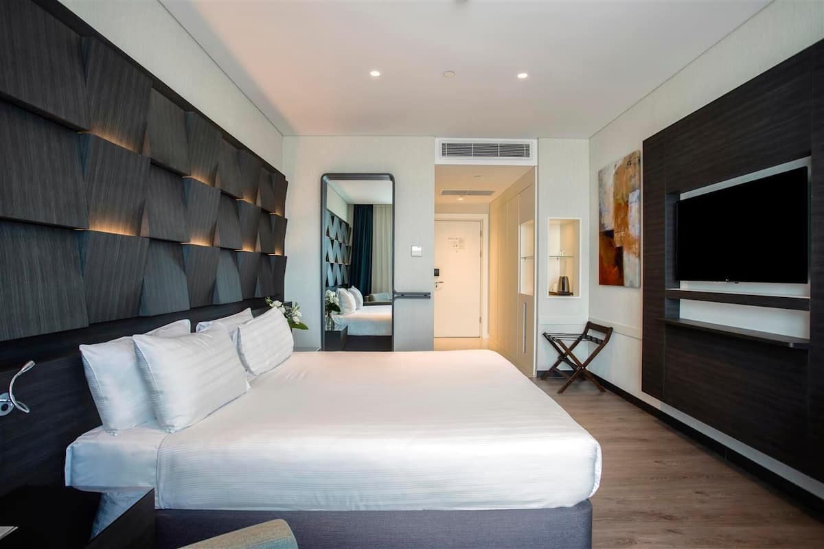 A modern hotel room with a large bed, a TV, and a walk-in closet.