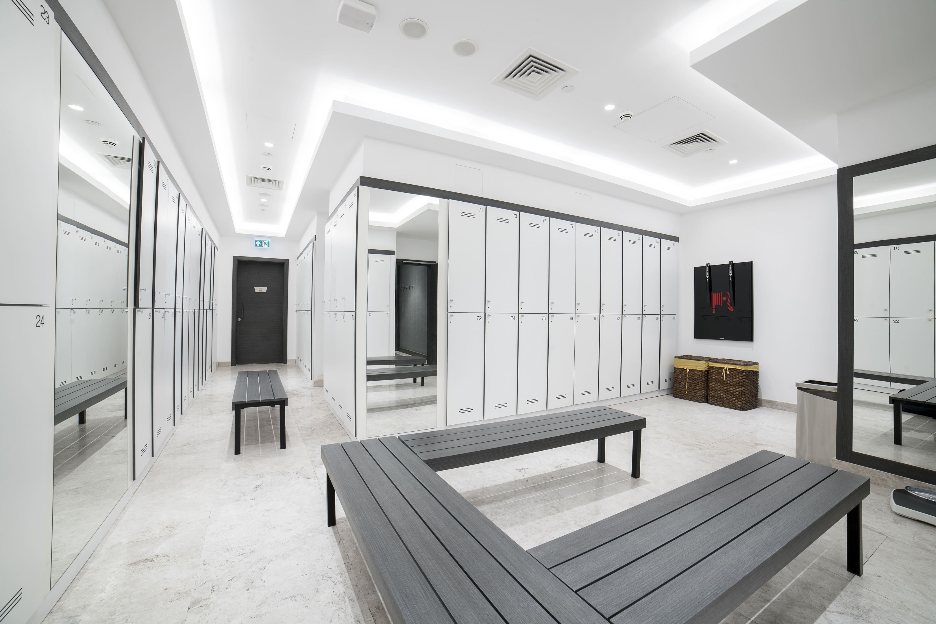 A modern locker room with benches, lockers, and a mirror.