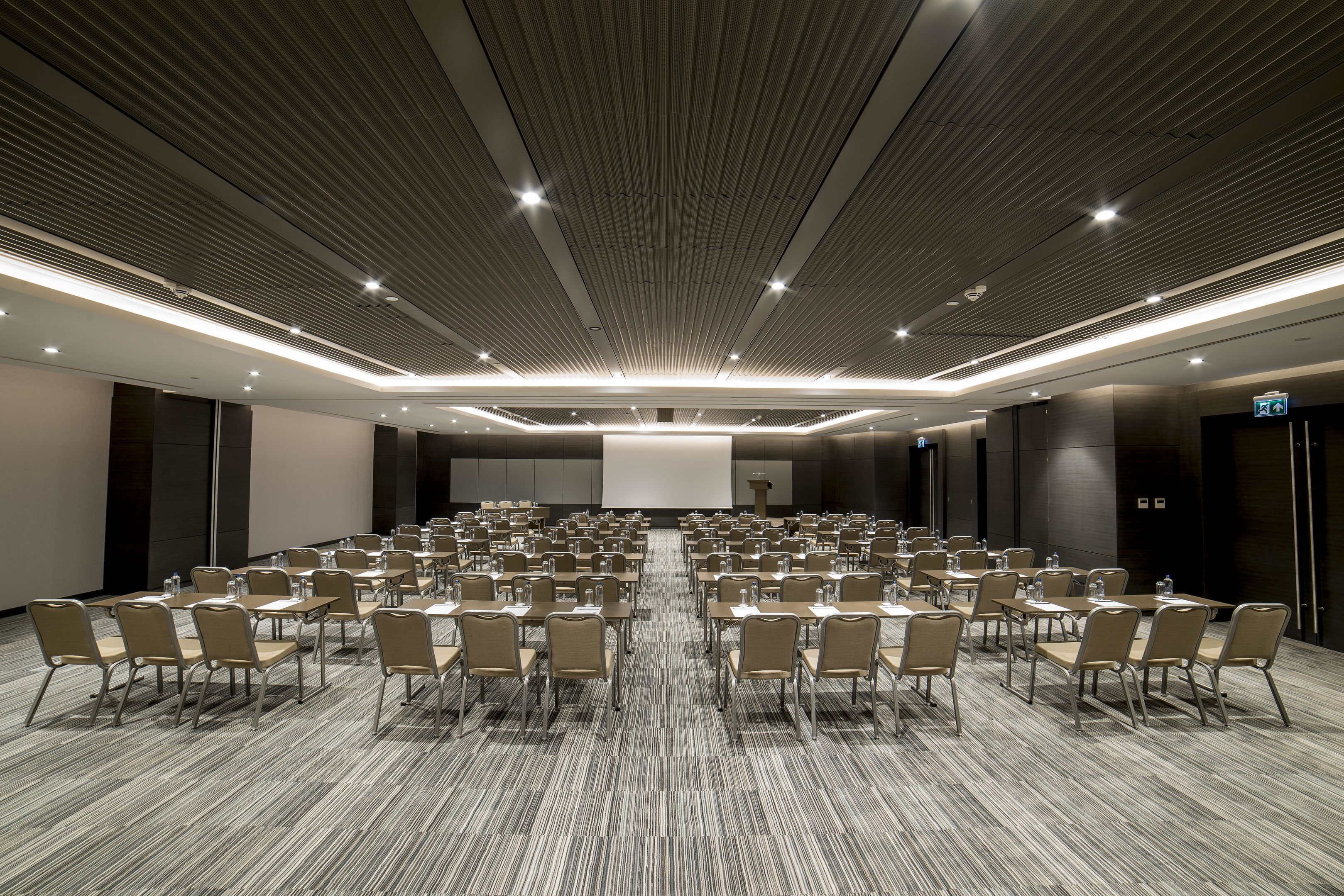 A conference room with rows of chairs, a large screen at the front, and a modern ceiling design.