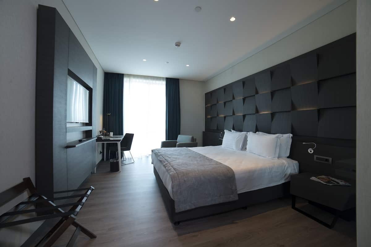 A modern hotel room with a large bed, a desk, and a chair.