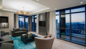 A modern living room with a sofa, armchair, and coffee table, large windows with a city view, and a flat-screen TV mounted on the wall. - Wish More Hotel Istanbul (Istanbul)