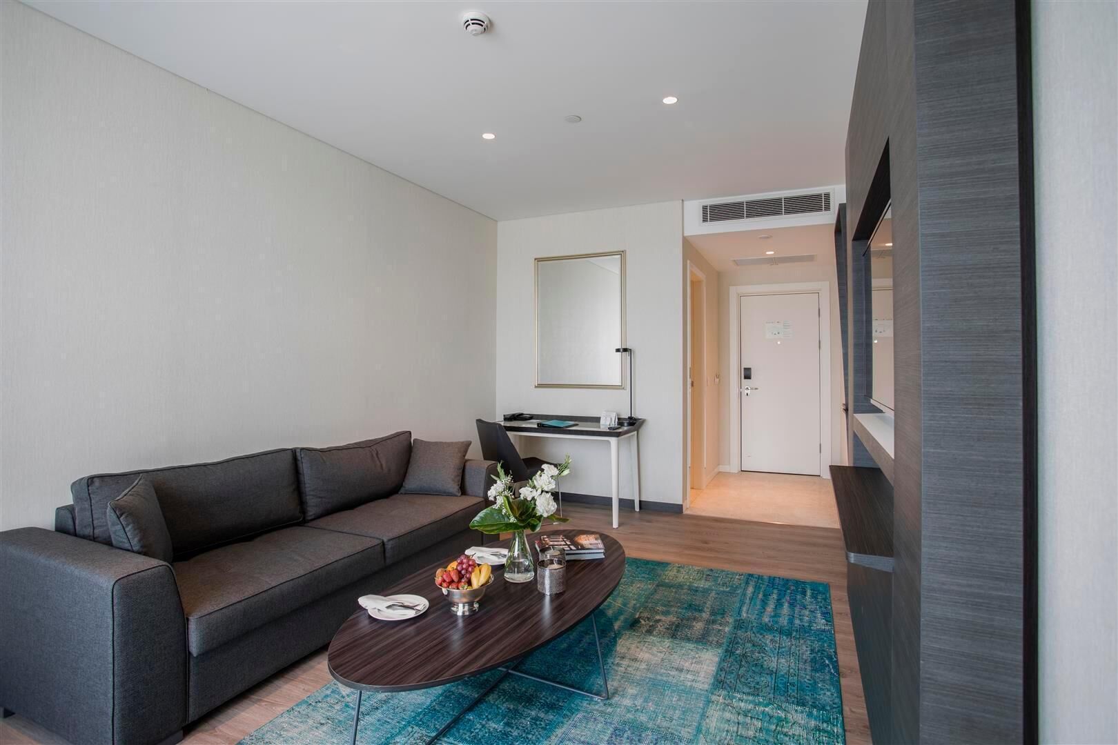 Una sala de estar moderna con un sofá gris, una mesa de centro con frutero y un tapete azul.