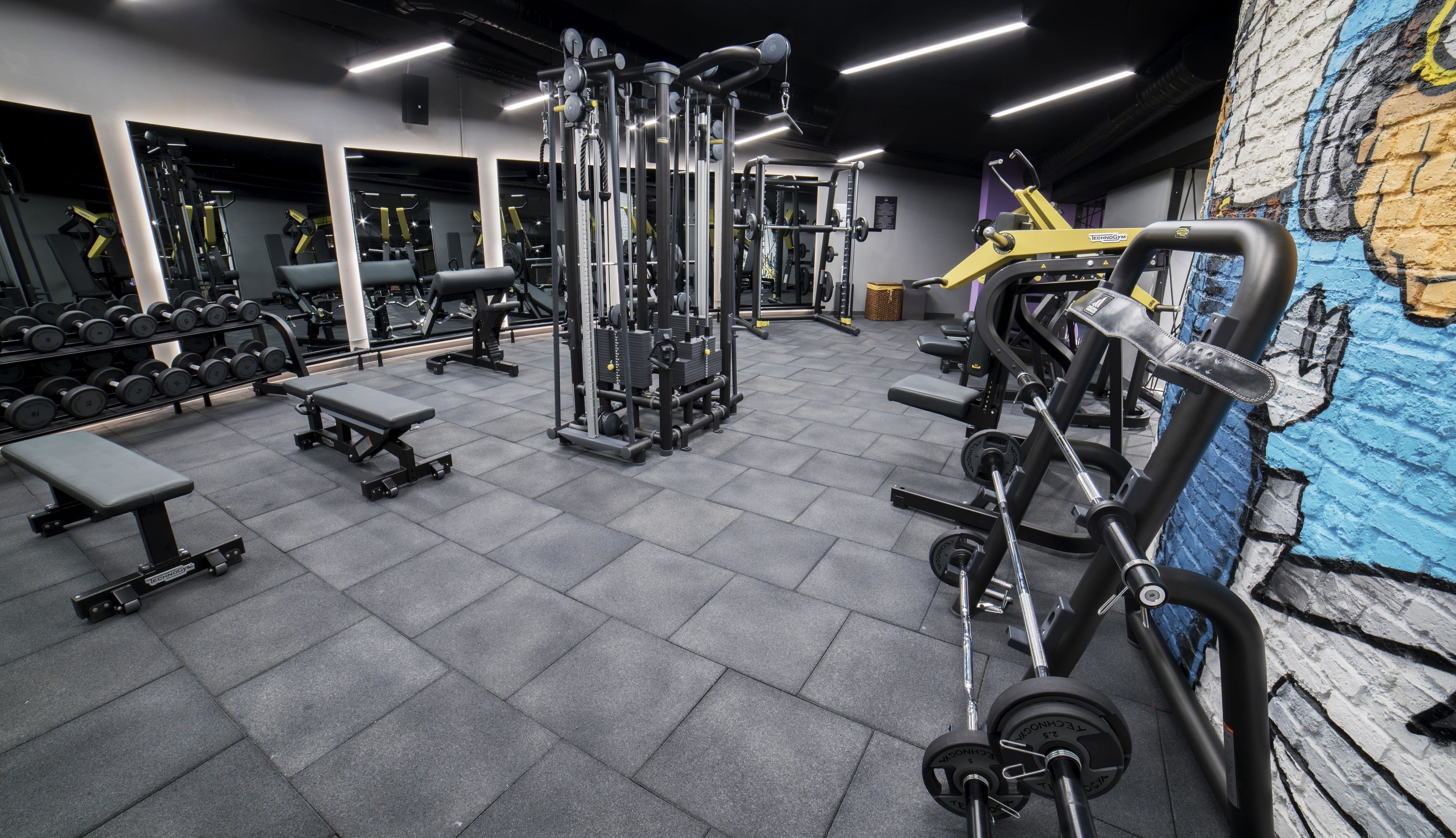 Une salle de sport équipée de divers appareils d’exercice, de miroirs et de bancs.
