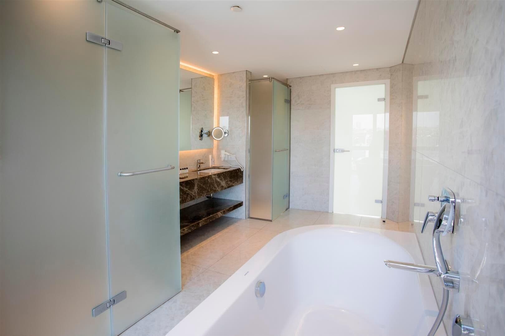 Une salle de bain moderne dotée d’une grande baignoire, d’une douche à parois de verre et d’un meuble-lavabo avec un plan de travail en marbre.