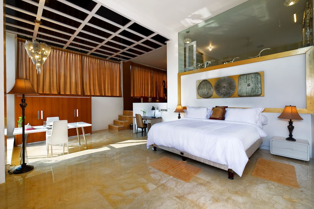 A modern bedroom with a large bed, a desk, and a chair. There is a staircase leading to an upper level.