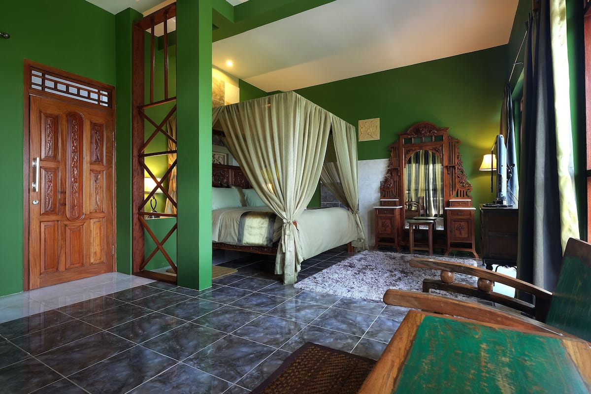 A room with a bed, a wooden wardrobe, a green wall, and a tiled floor.