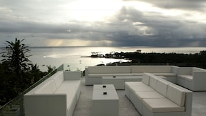 Un área de estar moderna al aire libre con vista al mar y un cielo nublado.
