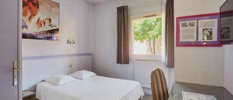 A bedroom with a single bed, a desk, a chair, a window with curtains, and a poster on the wall.