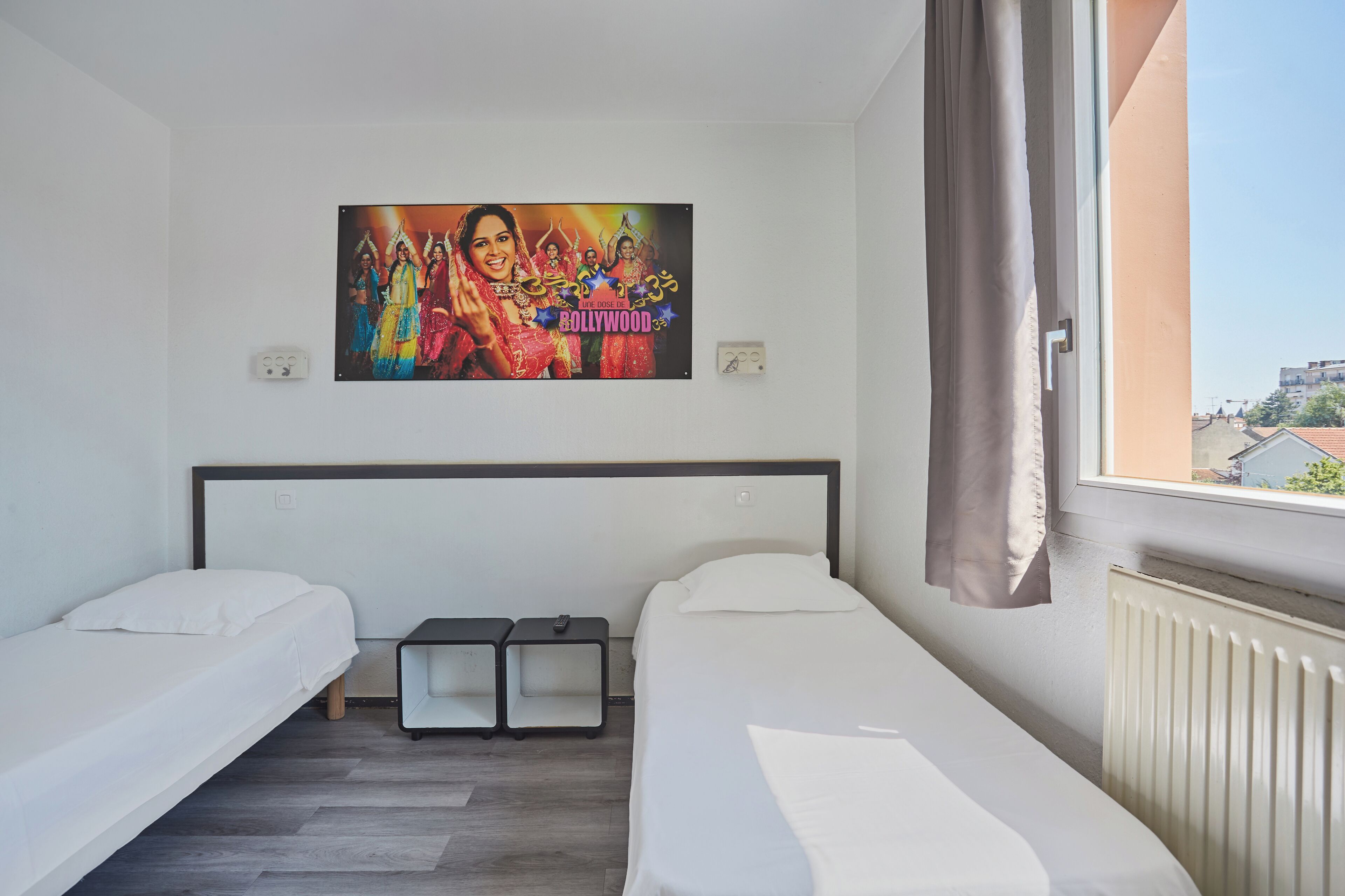 Habitació d'hotel amb dos llits individuals, una taula petita, televisió penjada a la paret i una finestra amb cortines.