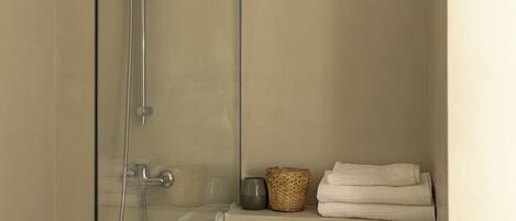 A shower with a glass door, a towel rack with folded towels, and a basket.