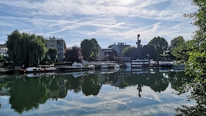 Un río tranquilo con barcos amarrados, rodeado de edificios y árboles.
