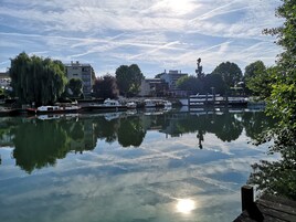 Un río tranquilo con barcos amarrados, rodeado de edificios y árboles.