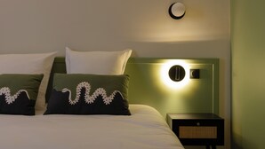 A neatly made bed with two pillows, a bedside table with a lamp, and a wall-mounted light fixture.