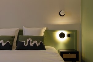 Una cama bien hecha con dos almohadas, una mesita de noche con una lámpara y un aplique de pared.