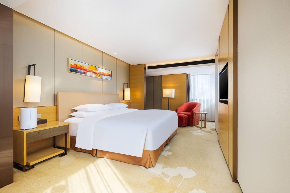 Ein Hotelzimmer mit einem großen Bett, Nachttischen, einem roten Sessel, einem kleinen Tisch und einem Fernseher.