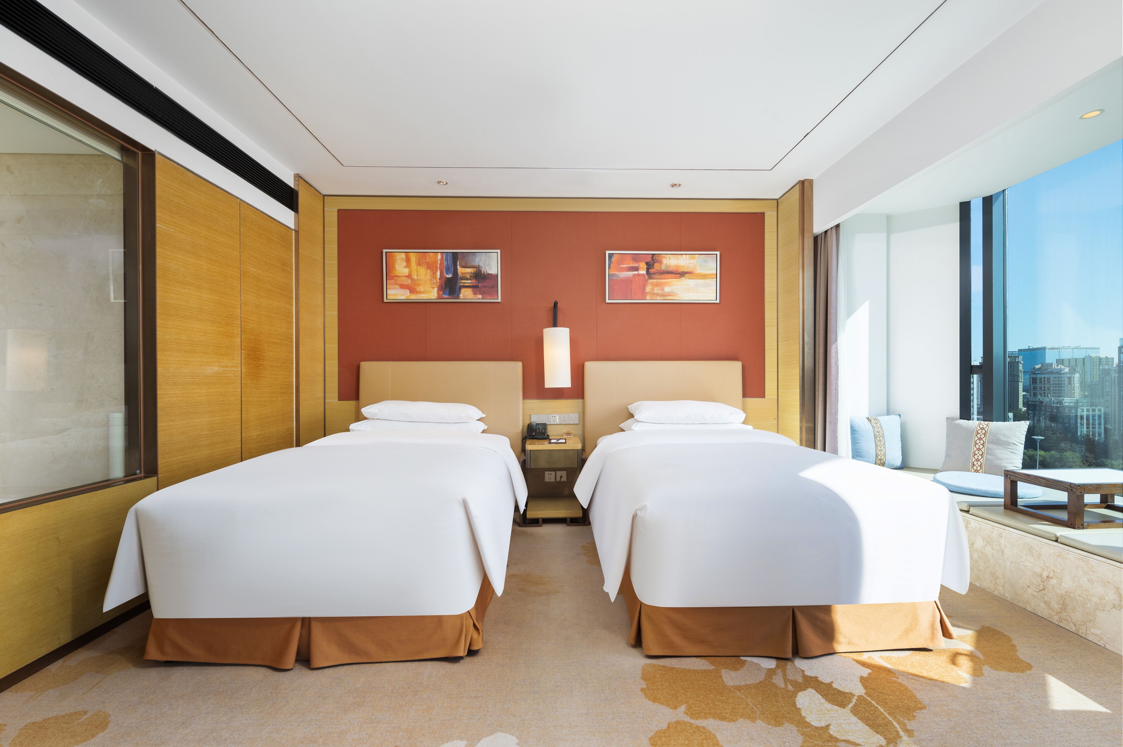 Habitación de hotel con dos camas, un ventanal grande con vista a la ciudad y obras de arte en la pared.