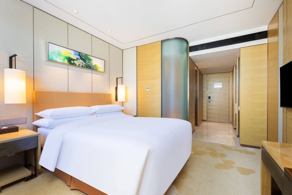 Ein Hotelzimmer mit einem großen Bett, Nachttischlampen, einem Flachbildfernseher und einem Gemälde an der Wand.