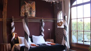 Ein Himmelbett mit weißen Leinentüchern, ein Giraffenbild an der Wand und Blick auf Grün hinter einem großen Fenster.