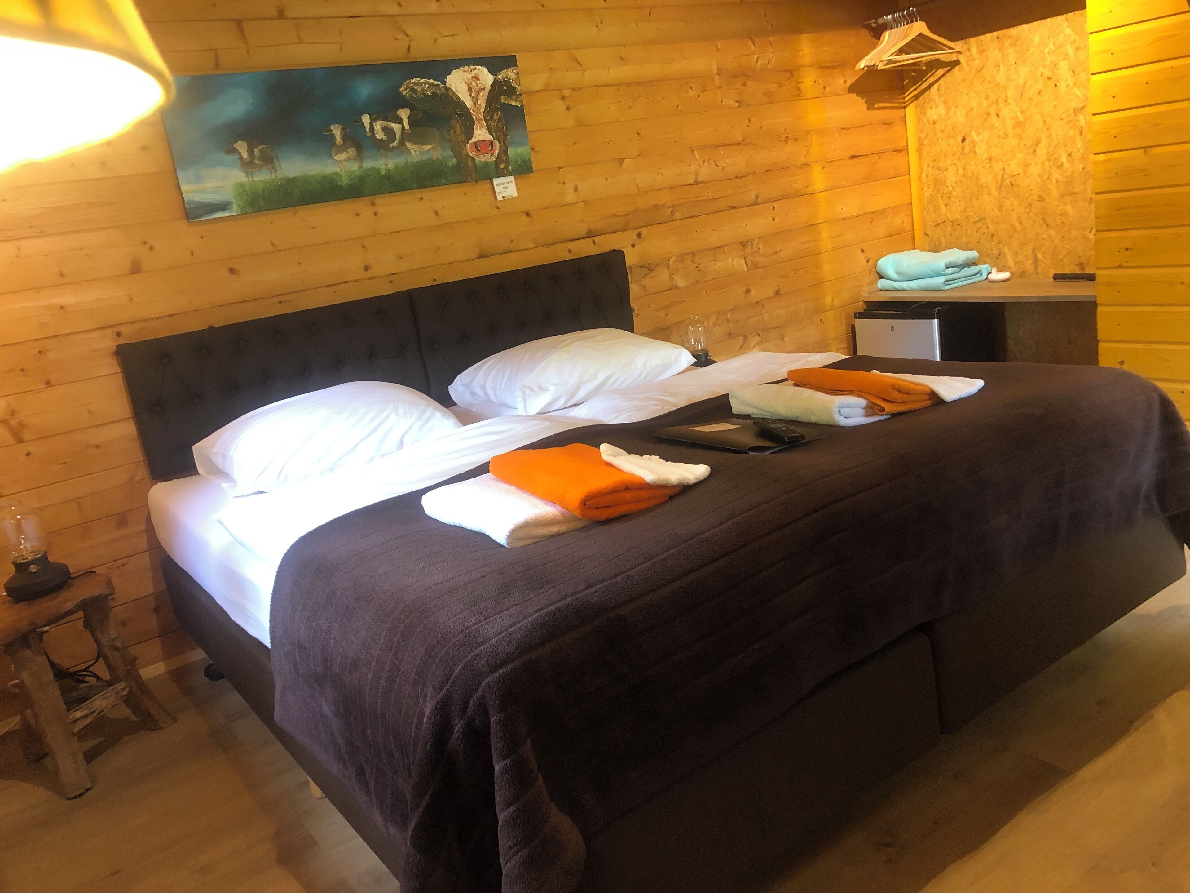 A wooden room with a bed, pillows, a blanket, and a painting on the wall.