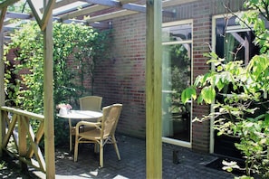 A covered patio with a table and chairs, a brick wall, and a glass door. - Boutique Hotel Nieuw Beusink (Winterswijk)