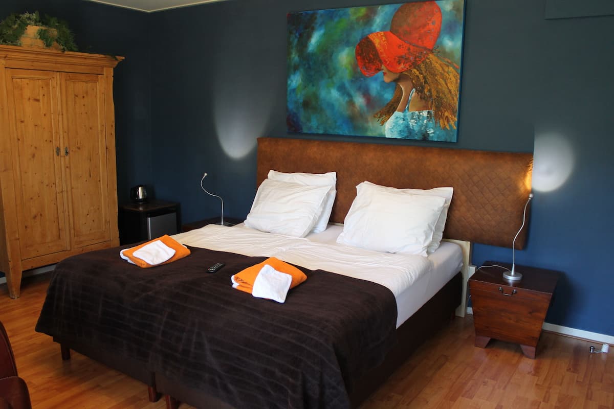 Quarto com uma cama grande, um guarda-roupa de madeira, uma mesinha de cabeceira e um quadro na parede.
