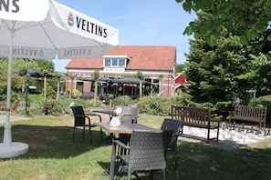 An outdoor seating area with tables and chairs, a chessboard, and umbrellas with the name "VELTINS". - Boutique Hotel Nieuw Beusink (Winterswijk)